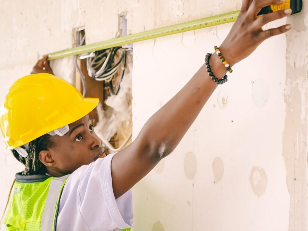 Woman in Yellow Hardhat Measuring the Wall 